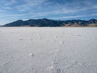 an empty area with a mountain in the distance and some footprints in the sand on it