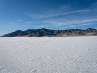 an empty area with a mountain in the distance and some footprints in the sand on it