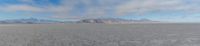 a desert with snow covered mountains in the distance and fog coming off of it in the sky