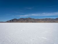 some large mountains and some snow and water on some flat ground with blue skies and one of them in the background