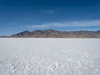 some large mountains and some snow and water on some flat ground with blue skies and one of them in the background