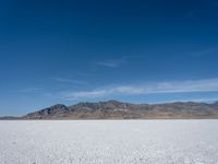 some large mountains and some snow and water on some flat ground with blue skies and one of them in the background