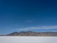 some large mountains and some snow and water on some flat ground with blue skies and one of them in the background