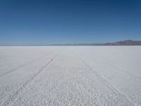 a wide open plain with some snow in the distance and mountains in the distance behind it