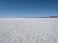 a wide open plain with some snow in the distance and mountains in the distance behind it