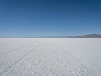 a wide open plain with some snow in the distance and mountains in the distance behind it