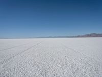 a wide open plain with some snow in the distance and mountains in the distance behind it