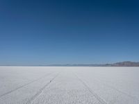 a wide open plain with some snow in the distance and mountains in the distance behind it