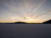 the sun is going down in the sky above snow covered desert area at dusk time