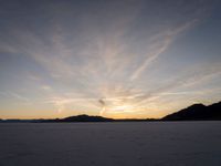 the sun is going down in the sky above snow covered desert area at dusk time