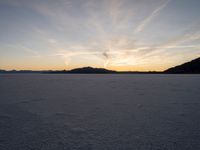 the sun is going down in the sky above snow covered desert area at dusk time