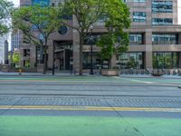 the green paint is painted on a bike path in front of an office building and large, trees