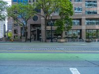 the green paint is painted on a bike path in front of an office building and large, trees