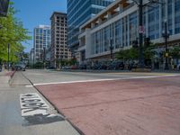 the green paint is painted on a bike path in front of an office building and large, trees