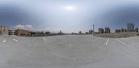 a fisheye image of a parking lot with trees in the distance, city buildings in the foreground and sky