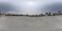 a concrete parking lot with some buildings in the background and blue skies overhead with low clouds