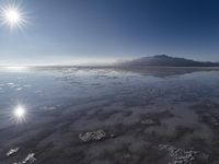 the sun shines above the horizon and water and rock formations along the shore line