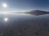 the sun shines above the horizon and water and rock formations along the shore line