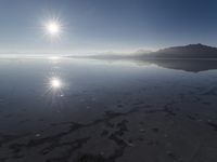 the sun shines above the horizon and water and rock formations along the shore line