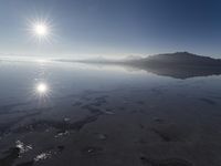 the sun shines above the horizon and water and rock formations along the shore line