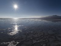 the sun shines above the horizon and water and rock formations along the shore line