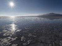 the sun shines above the horizon and water and rock formations along the shore line