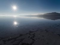 the sun shines above the horizon and water and rock formations along the shore line