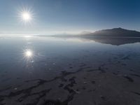 the sun shines above the horizon and water and rock formations along the shore line