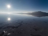 the sun shines above the horizon and water and rock formations along the shore line