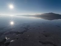 the sun shines above the horizon and water and rock formations along the shore line