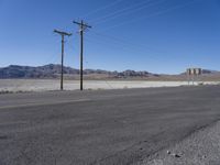 a road with power lines above the side in a desert area, the mountains in the background