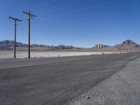 a road with power lines above the side in a desert area, the mountains in the background