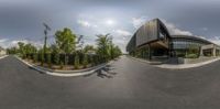 a fish eye lens of some kind with trees and buildings in the background and two people riding their bikes behind the building