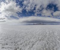 large expanse of flat salt under a cloudy blue sky and mountains and mountain peaks behind the salt