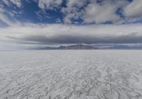 large expanse of flat salt under a cloudy blue sky and mountains and mountain peaks behind the salt