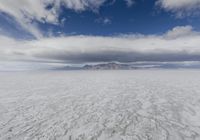 large expanse of flat salt under a cloudy blue sky and mountains and mountain peaks behind the salt