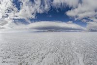 large expanse of flat salt under a cloudy blue sky and mountains and mountain peaks behind the salt