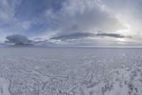 a wide view of an open ice field in the middle of winter with lots of snow in front of clouds