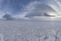 a wide view of an open ice field in the middle of winter with lots of snow in front of clouds