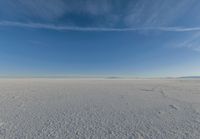 blue sky with clouds and sun in it over open space with snow covered land in foreground