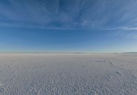 blue sky with clouds and sun in it over open space with snow covered land in foreground