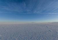 blue sky with clouds and sun in it over open space with snow covered land in foreground