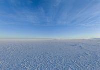 blue sky with clouds and sun in it over open space with snow covered land in foreground