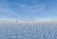 a lone person in the middle of a vast open field in snow against a blue sky and some clouds