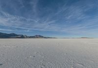 two people standing in a snow field with mountains behind them in the distance in blue skies