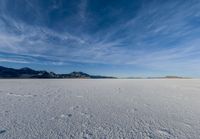 two people standing in a snow field with mountains behind them in the distance in blue skies