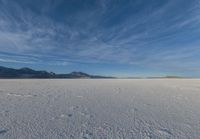 two people standing in a snow field with mountains behind them in the distance in blue skies