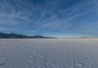 two people standing in a snow field with mountains behind them in the distance in blue skies