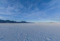 two people standing in a snow field with mountains behind them in the distance in blue skies