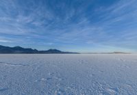 two people standing in a snow field with mountains behind them in the distance in blue skies